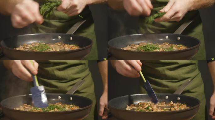 男主厨在热煎锅里将绿莳萝添加到炸蘑菇中。厨师用手摘下莳萝叶，然后将它们和蘑菇一起扔进锅里。