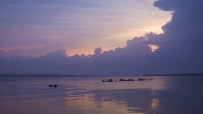 平静的海面上的紫色日落，明亮的阳光照耀着傍晚的云层