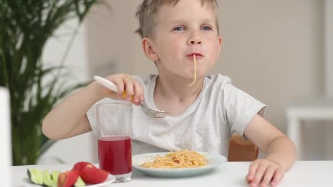 厨房里的男孩在家里吃意大利面时微笑着。好孩子食欲概念