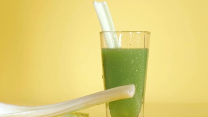 美味的有机芹菜汁在玻璃上的黄色背景。