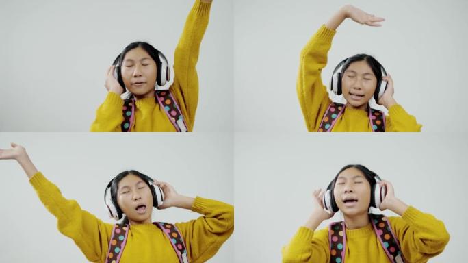 快乐的亚洲女孩使用耳机，在灰色背景下唱歌跳舞，教育生活方式理念。