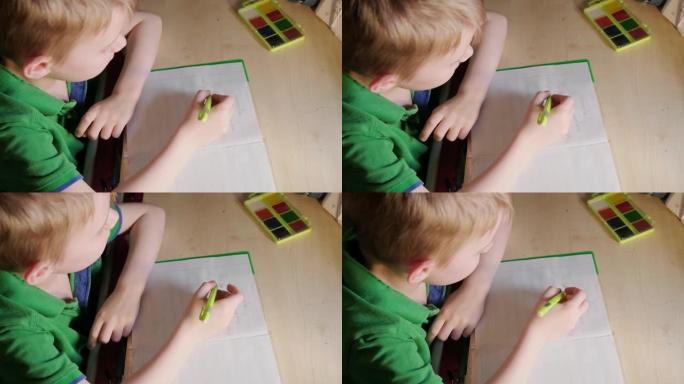 一个小男孩正在桌边做作业。在笔记本上写学校的作业。