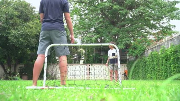 年轻的亚洲老大哥踢足球进行户外锻炼，周末在花园里与小弟弟一起休闲活动，低角度视角: 大男孩作为进球球