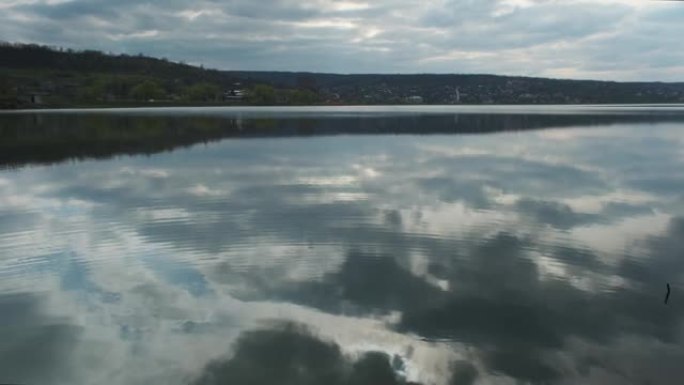 河流或湖泊景观，在水中反射多云的天空。晚上或早上平静的水面的波纹