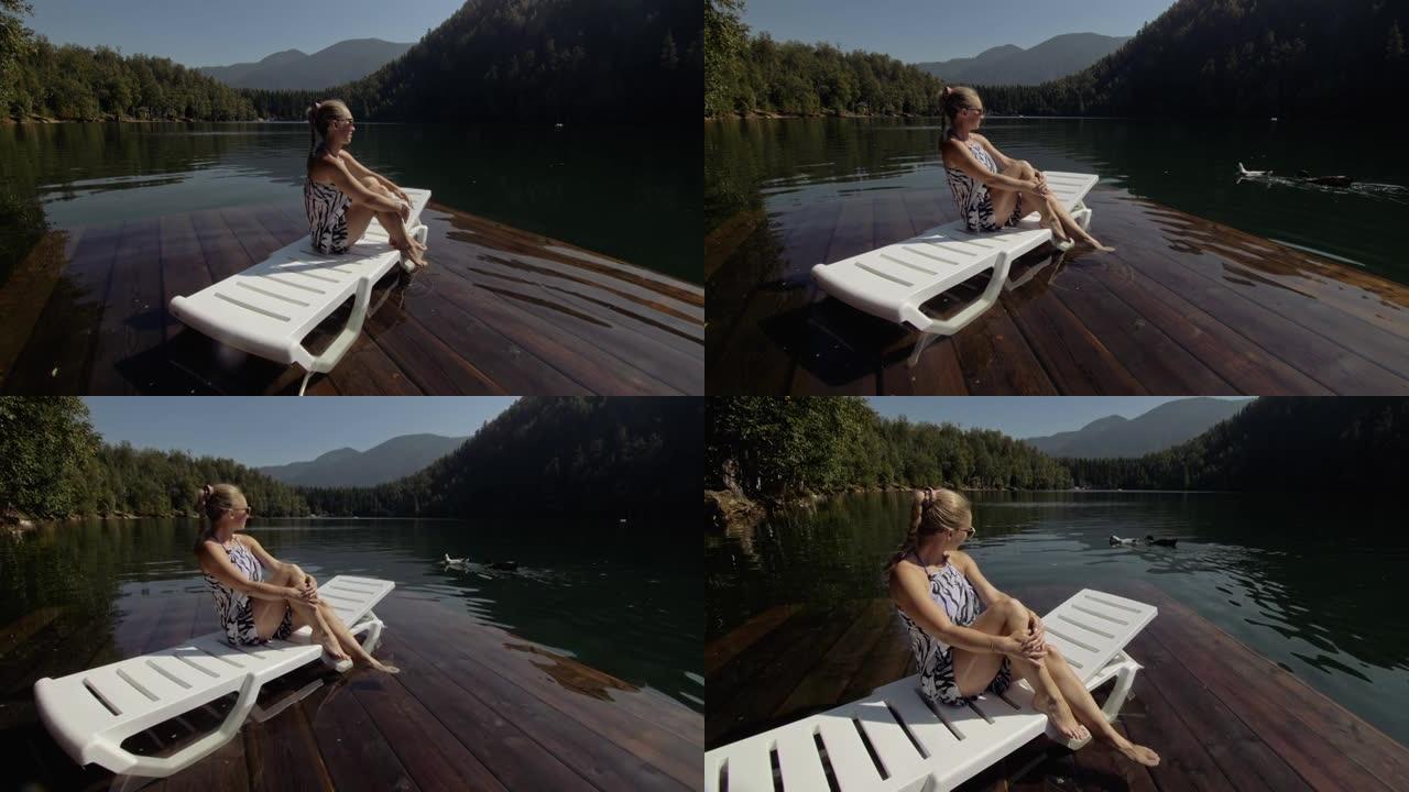 女人躺在太阳镜和波西米亚丝绸披肩的日光浴床上。女孩在洪水木水下码头上休息。湖里铺满了水。