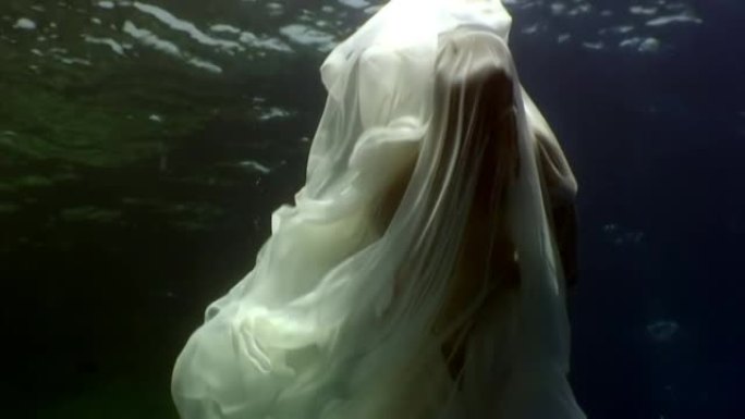 蓝色水底背景上白布的年轻女子水下模型。