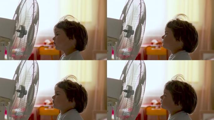 男孩站在范面前。暑假在家享受电风扇带来的凉风的孩子。用电风扇冷却器冷却自己的通风机前受热高温。
