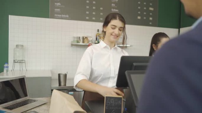穿着围裙的年轻中东女性咖啡师通过扫描手机屏幕上的QR码，在柜台与顾客交谈，咖啡厅收银员来收取订单付款