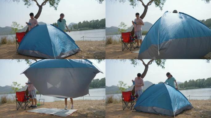 亚洲儿童试图在户外湖泊附近的地面上搭蓝色帐篷，生活方式概念。