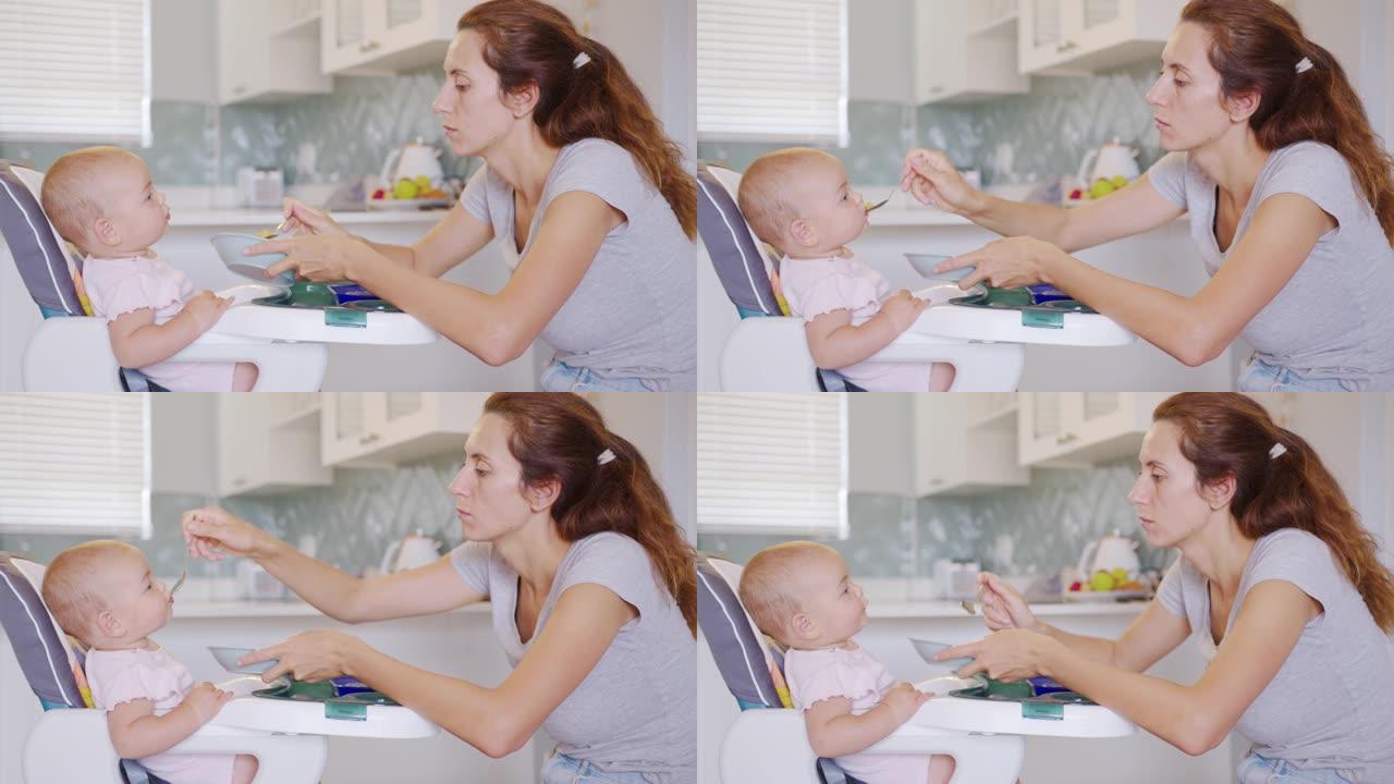 母亲用婴儿勺子给婴儿食物，孩子心甘情愿地吃东西。可爱的小宝贝吃她的晚餐。