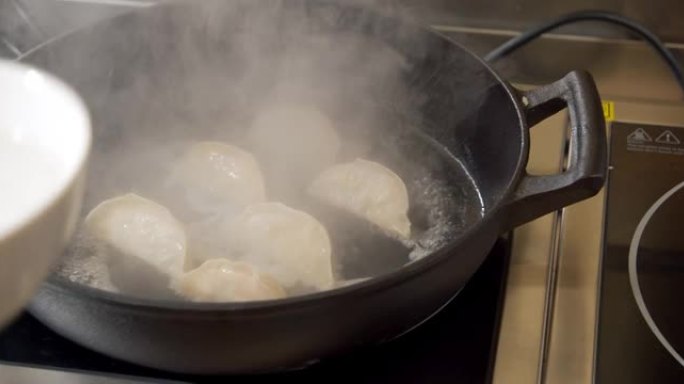 男厨师双手戴着黑手套在热煎锅上准备美味饺子的特写镜头