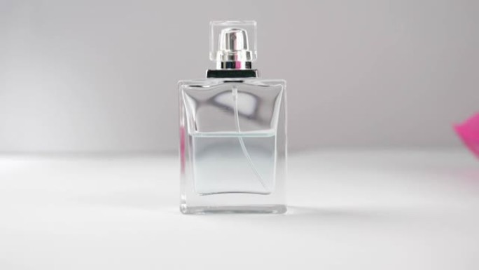 带有青色香水或精油的平面瓶子在灰色背景的白色桌子上。粉红色和米色的织物从镜头中飘动。香气和气味的概念