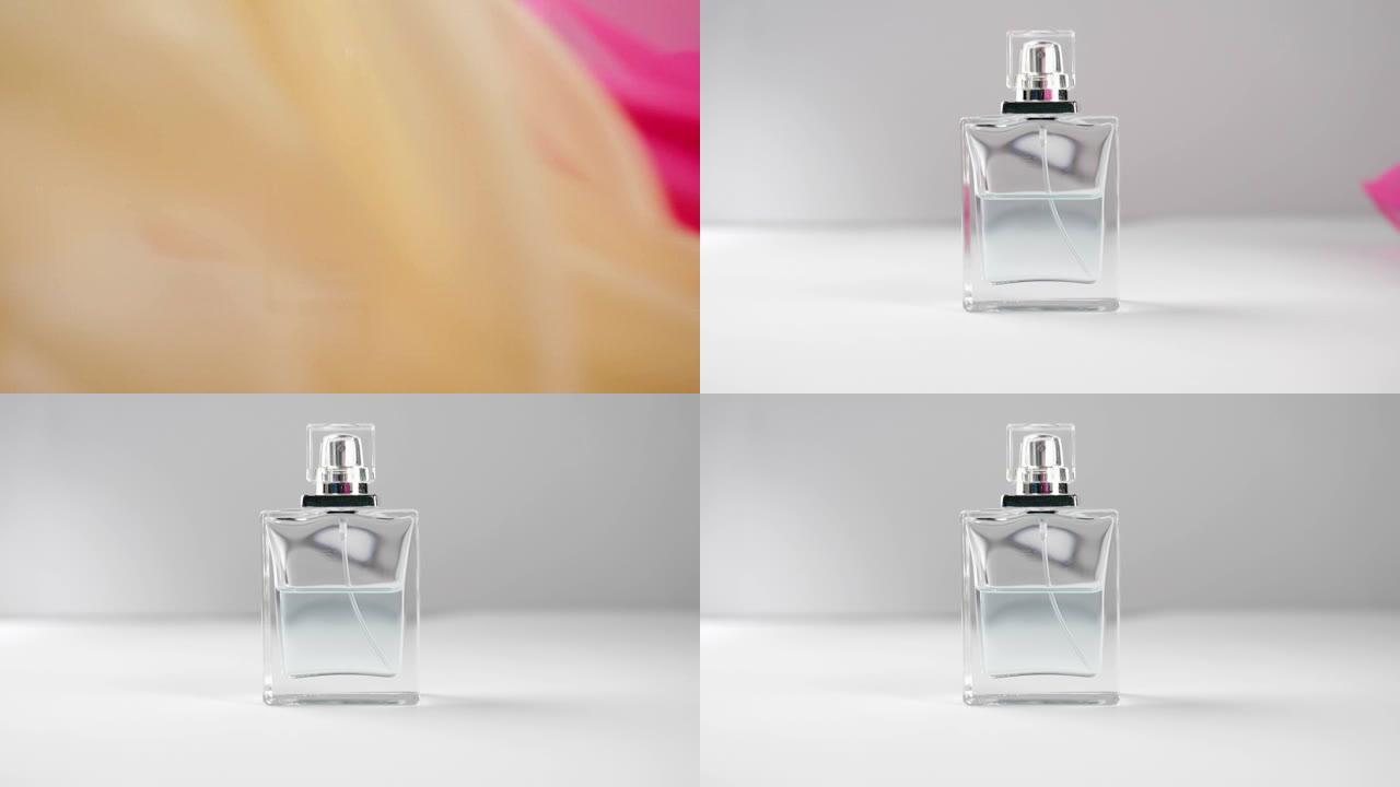 带有青色香水或精油的平面瓶子在灰色背景的白色桌子上。粉红色和米色的织物从镜头中飘动。香气和气味的概念