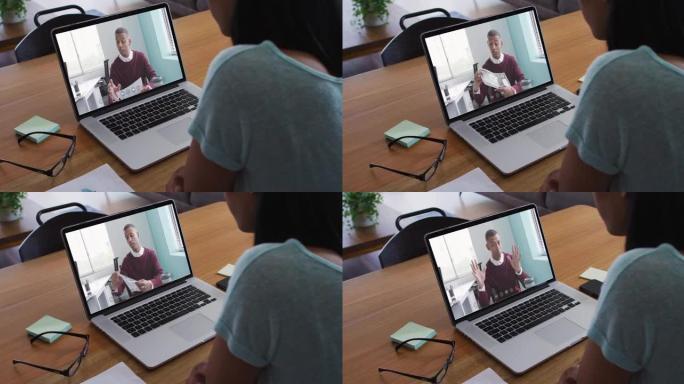 混血女商人坐在办公桌前，用笔记本电脑与男同事进行视频通话