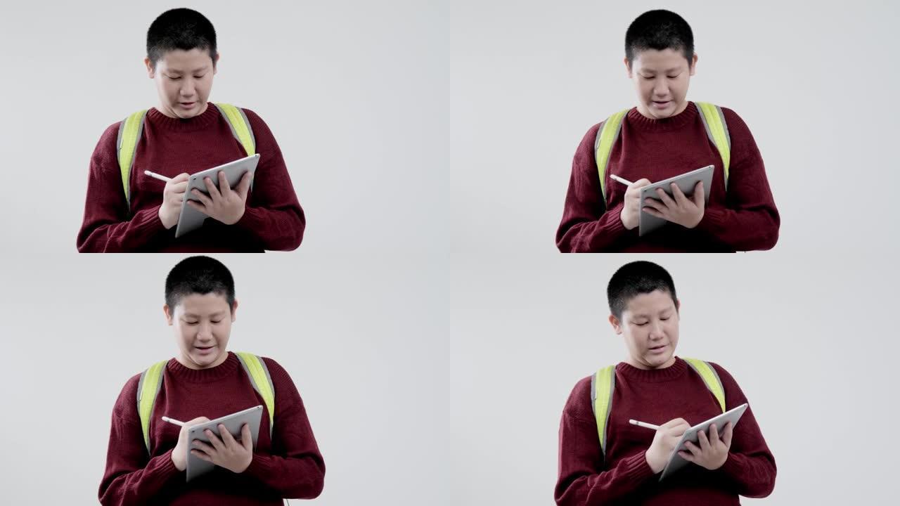 穿着红色毛衣的亚洲男生在灰色背景下用数字平板电脑写字笔记，教育生活方式理念。