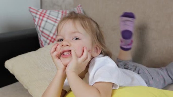 一个小女孩躺在黄色枕头上用手指抠嘴的大画像。他做鬼脸。