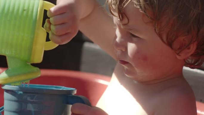 男孩将玩具喷壶中的水倒入塑料壶中