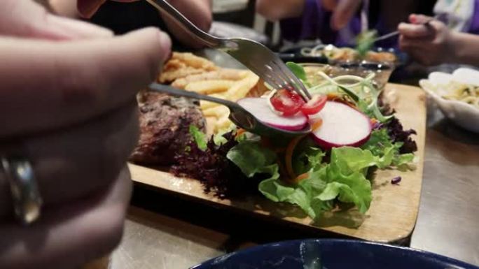 女人用叉子在餐厅的木托盘里拿沙拉蔬菜吃