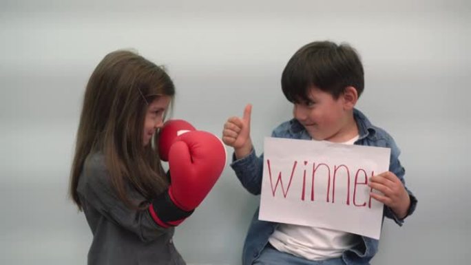 女孩展示拳击手套，男孩拿着一张纸，上面写着题词获胜者，并向班级展示孩子们在灰蓝色背景上举着一个带有获