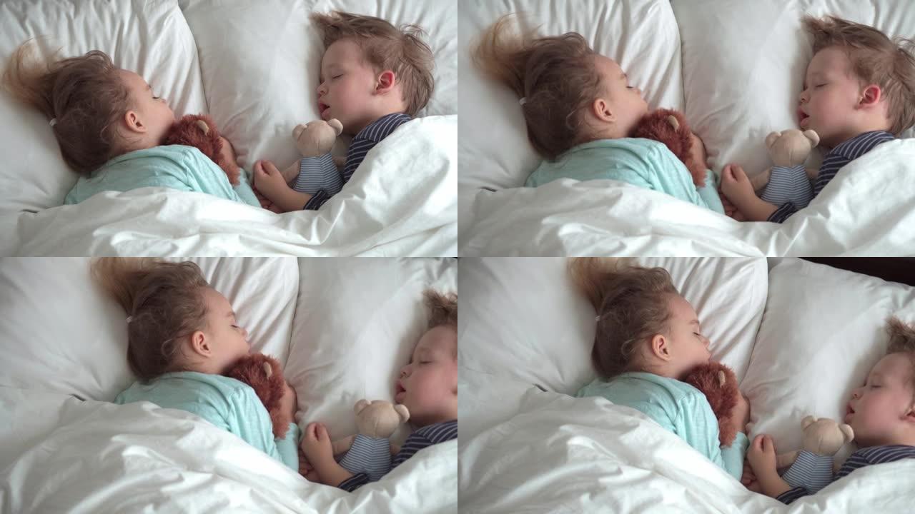正宗的肖像可爱的高加索小学龄前兄弟姐妹男婴和女孩在蓝色的睡眠与泰迪熊在白色的床上。午餐时间休息的孩子