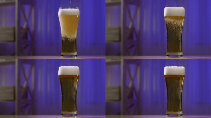 将冰镇啤酒倒入玻璃杯中。一杯带有气泡和厚厚的白色泡沫的啤酒站在蓝色模糊背景下的木制桌子上。慢动作。特
