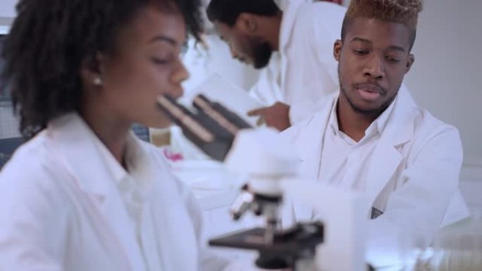 非洲民族，在实验室使用显微镜的女性医生。用防护面罩关闭脸部。背景团队
