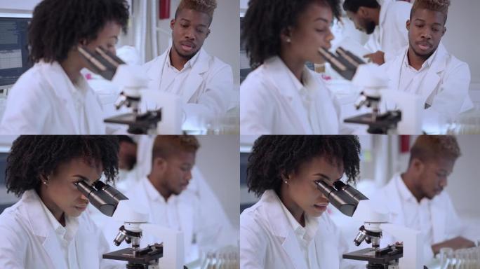 非洲民族，在实验室使用显微镜的女性医生。用防护面罩关闭脸部。背景团队
