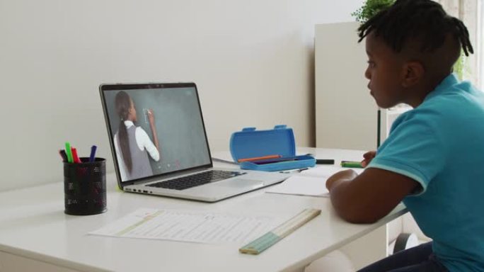 非裔美国男孩坐在桌子上使用笔记本电脑上在线课程