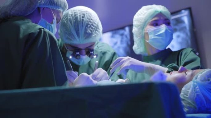 一名戴着双目放大镜的外科医生的低角度视角，致力于挽救她的性命，亚洲女性患者躺在医院手术室的床上延长寿