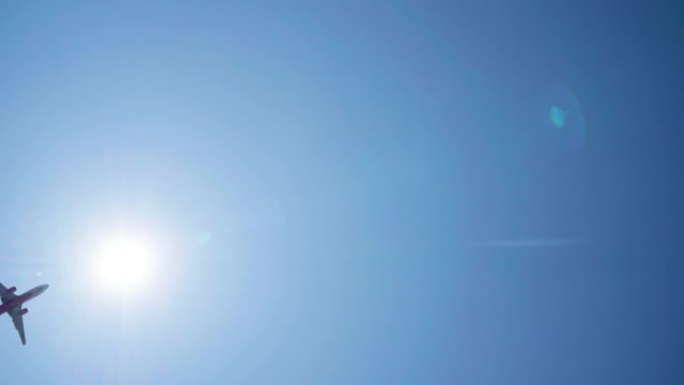 一架客机在明亮的蓝天背景下起飞或降落的仰视图，带有太阳光束的耀斑。航空航天或旅游工业4k概念镜头。
