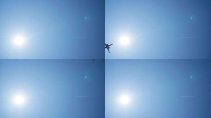 一架客机在明亮的蓝天背景下起飞或降落的仰视图，带有太阳光束的耀斑。航空航天或旅游工业4k概念镜头。