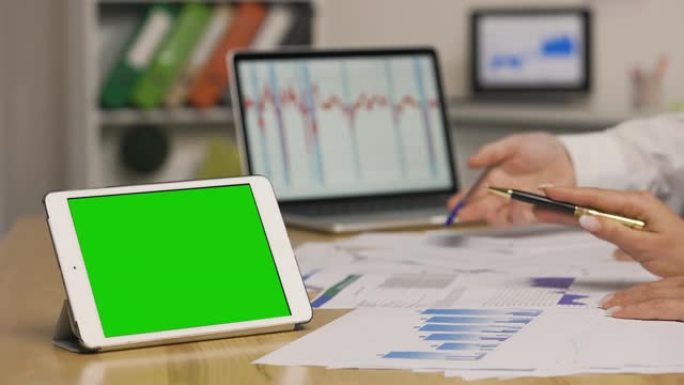 男人和女人使用笔记本电脑查看带有图表的论文。市场营销策略分析，股票市场交易。带绿屏色度键的平板电脑。