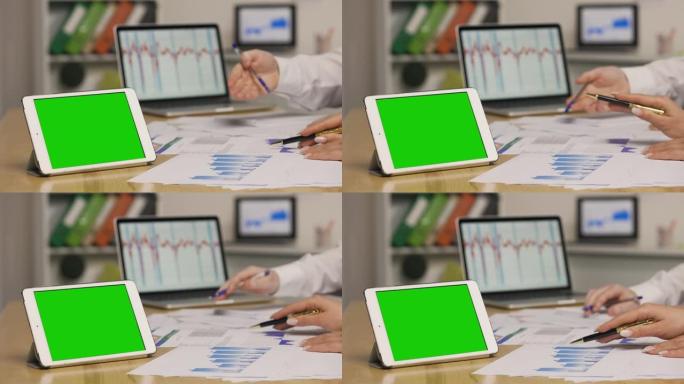 男人和女人使用笔记本电脑查看带有图表的论文。市场营销策略分析，股票市场交易。带绿屏色度键的平板电脑。