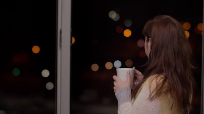 晚上靠近窗户的黑发女人喝热咖啡，看着车灯