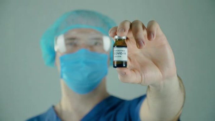 在细菌学实验室中，佩戴面部防护面罩的医疗科学家手持安瓿或瓶，并带有注射用抗冠状病毒moderna疫苗
