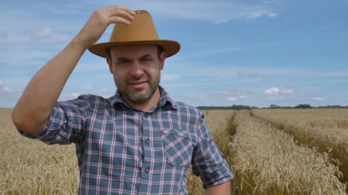 肖像高加索农民男子穿着帽子的格子衬衫看着相机。农田早晨景观农业。肖像农民留着帽子的男人站在麦田里。农