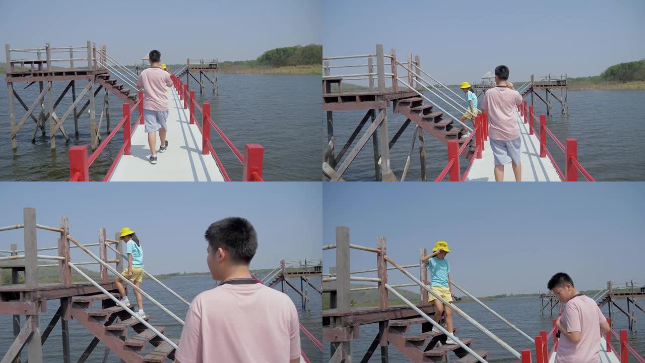 快乐的亚洲儿童走在湖上的桥上，在阳光明媚的日子里看着风景，生活方式的概念。