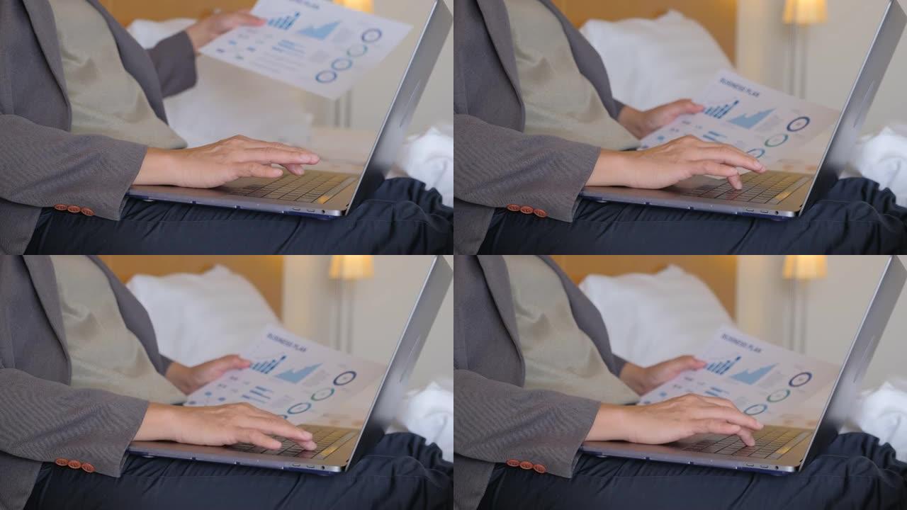 女商人穿着西装的特写手坐在酒店房间的床上，使用笔记本电脑在商务旅行之间工作