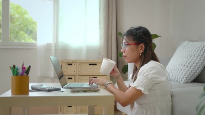 年轻的亚洲女性在检疫Covid 19大流行期间，在电脑笔记本电脑上滚动在社交媒体上搜索数据，在家工作