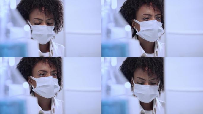 非洲民族，在实验室使用显微镜的女性医生。用防护面罩关闭脸部。浏览实验室玻璃器皿