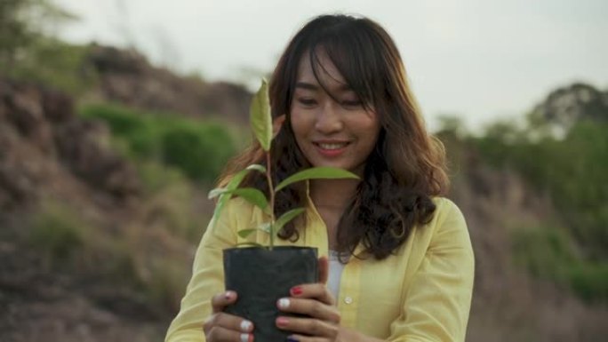 阳光明媚的日子，亚洲妇女在户外抱着植物微笑。
