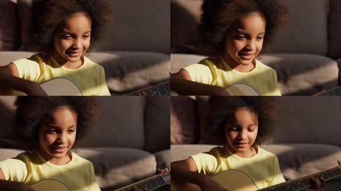 肖像小非洲裔美国女孩在明亮的阳光下弹吉他。十几岁的女孩坐在大厅的地板上，背景是明亮美丽的房间内部。慢