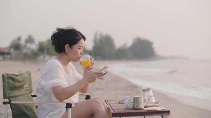 女人在智能手机上发短信，坐在沙滩上微笑。