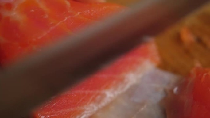 健康饮食海鲜欧米茄。男子在木板上切红鱼鲑鱼特写。厨师切红鱼，最美味的肉慢动作。宏观厨师切鲑鱼片，用于