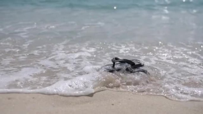 热带白色沙滩上的一双拖鞋和水浪的慢动作