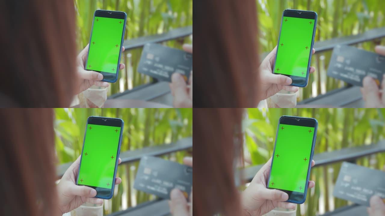 特写镜头，并放大手持色度键绿色屏幕和信用卡的女性手持智能手机，以慢动作拍摄的方式在咖啡馆进行在线购物