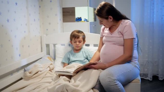 美丽的怀孕母亲晚上睡觉前给她躺在床上的大儿子读故事书。父母给孩子读书