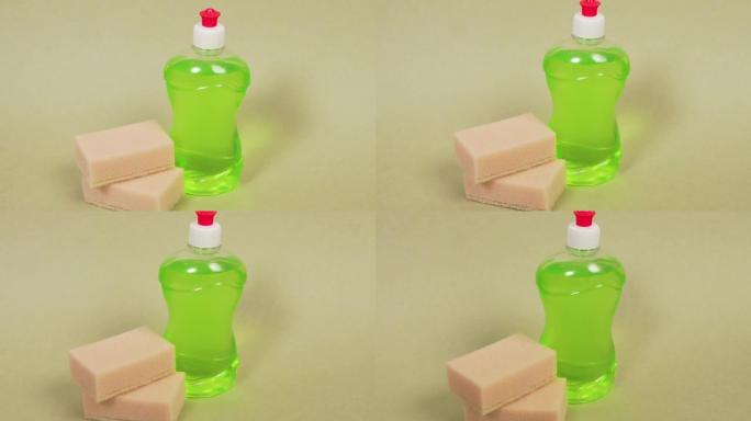 绿色洗洁精装在一个透明的瓶子和两个海绵里。浅色背景。