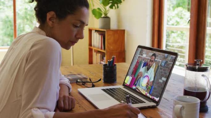 非裔美国妇女在家里用笔记本电脑与男同事进行视频通话时做笔记