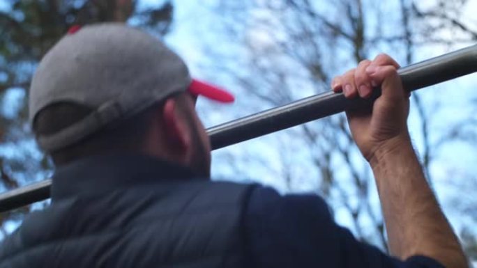 白人男性在体育锻炼期间在森林的户外酒吧锻炼引体向上